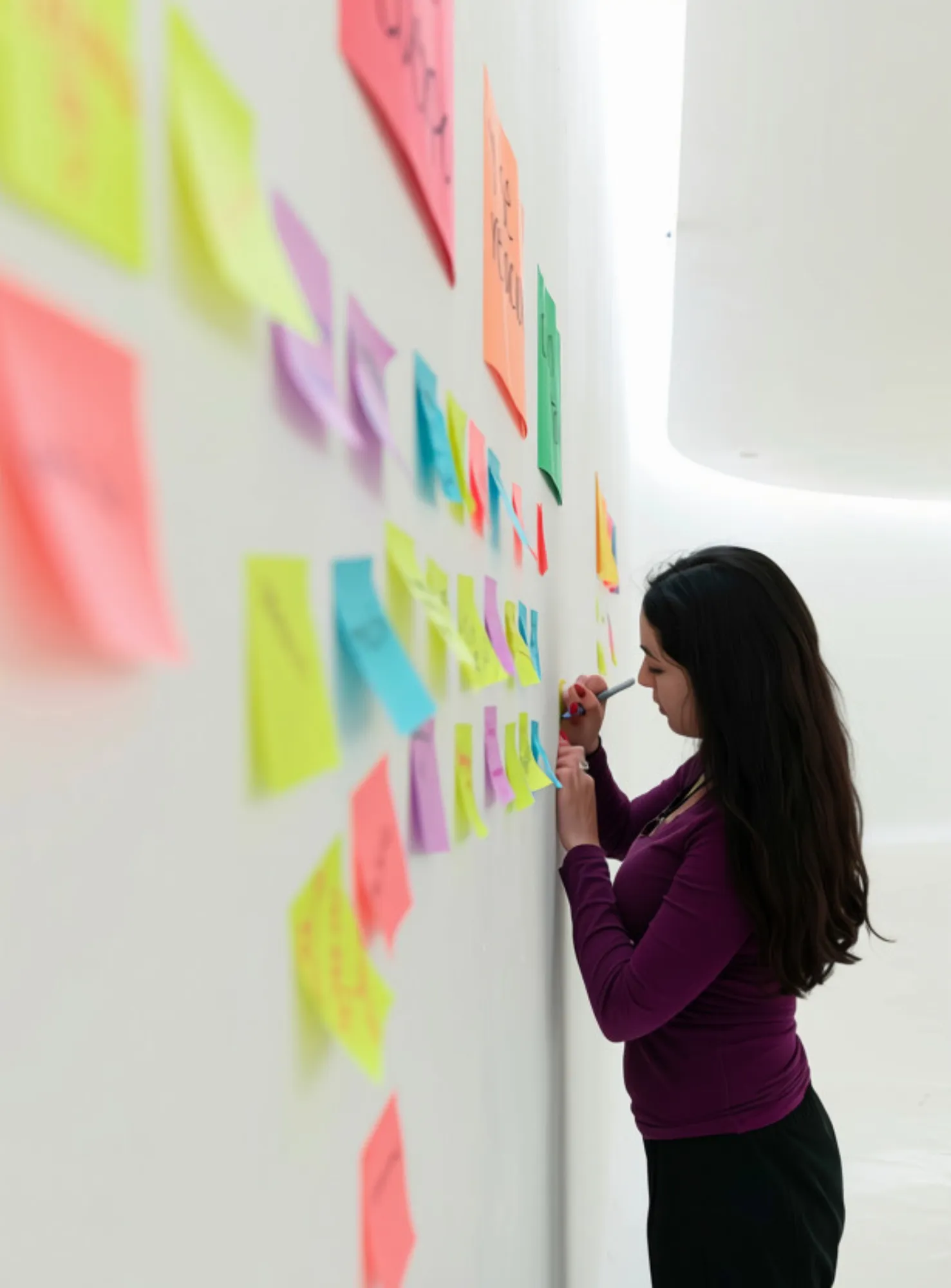 Joven escribiendo ideas en notas de colores pegadas en la pared